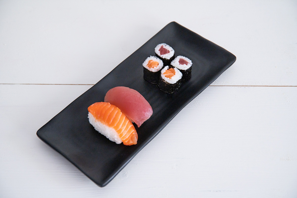 Zwei Nigiri Sushi neben vier Maki Sushi Rollen auf schwarzem Teller.