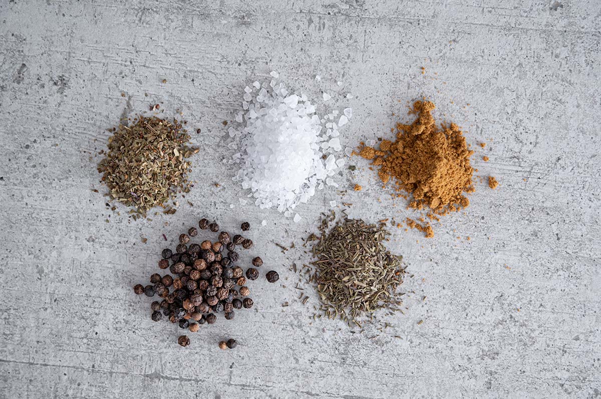 verschiedene Zutaten für das Grillgewürz wie Pfeffer, Salz und Currypulver lose nebeneinander verstreut.