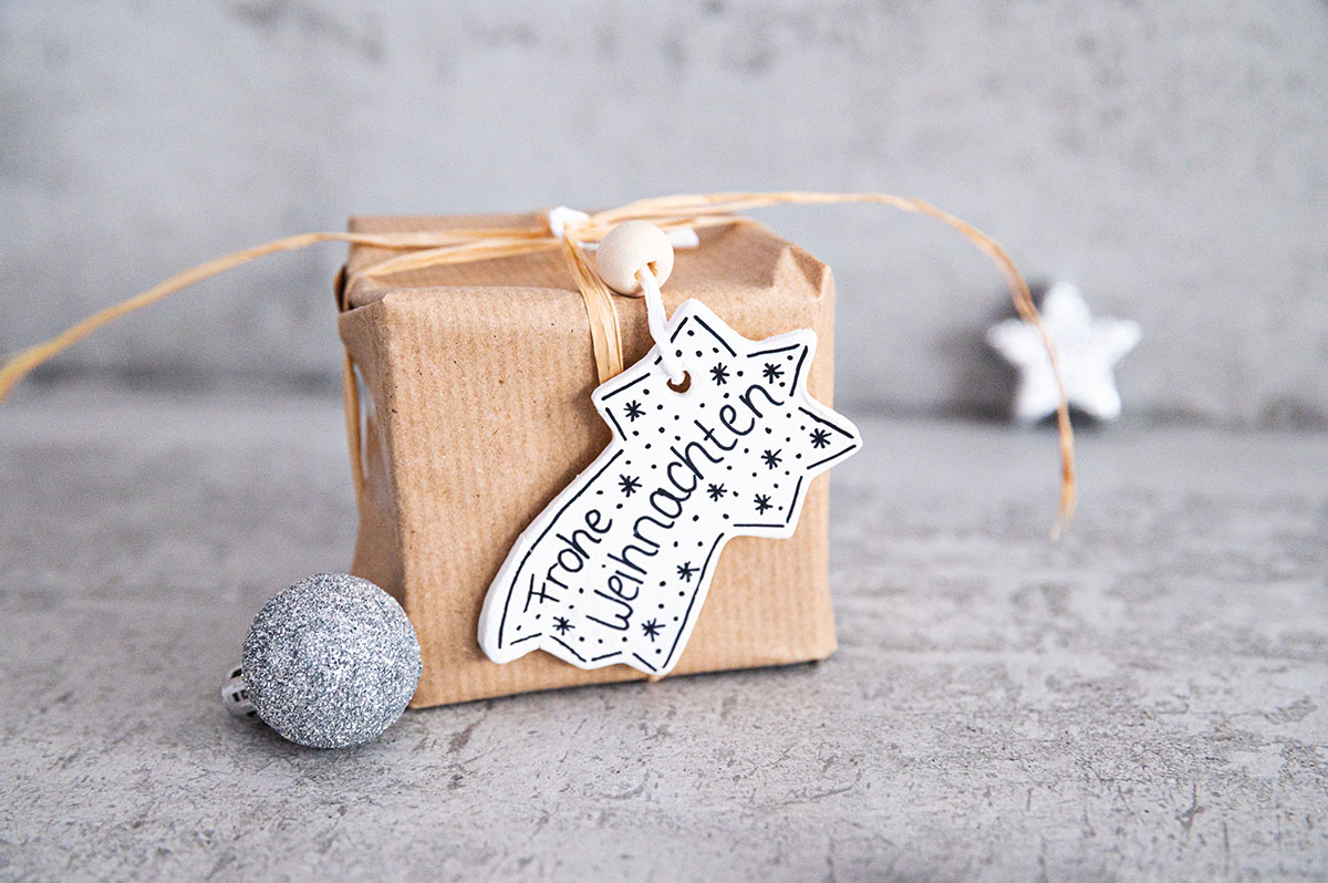 Einzelnes Mini-Geschenkpäckchen mit DIY ANhänger in Sternschnuppenform auf dem "Frohe Weihnachten" steht.