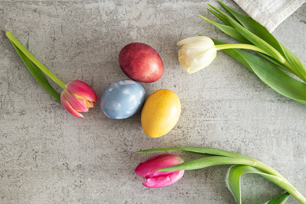 3 verschieden gefärbte Eier: Rot, Blau und Gelb. Daneben drei Tulpen als Dekoartikel.