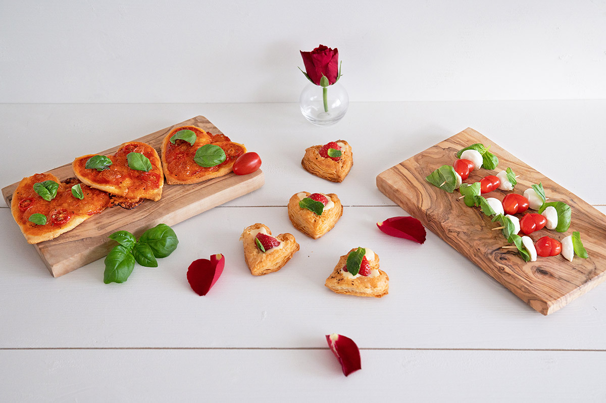 Alle genannten Valentinstag Snacks nochmal zusammen angerichtet, mit Rosenblättern als Deko verstreut.