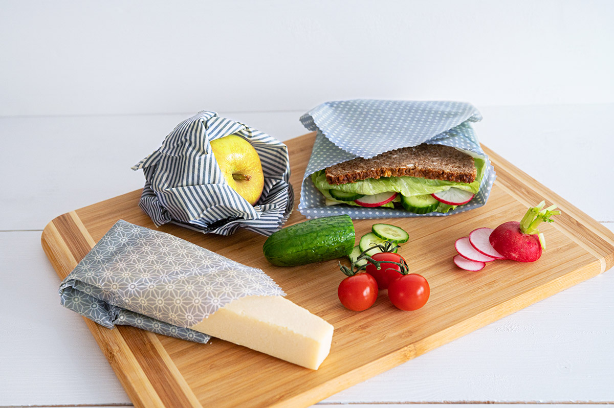 In Bienenwachs verpacktes Sandwich, Apfel nd Käse, daneben lose Tomaten, Gurken und Radieschen.